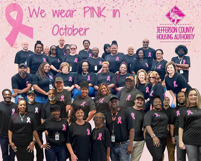 JCHA staff members are all gathered together wearing matching shirts that feature a breast cancer awareness ribbon. 