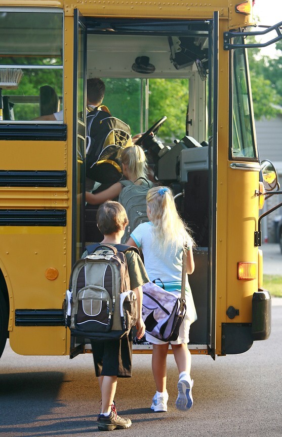 Children with backpacks getting on a school bus.