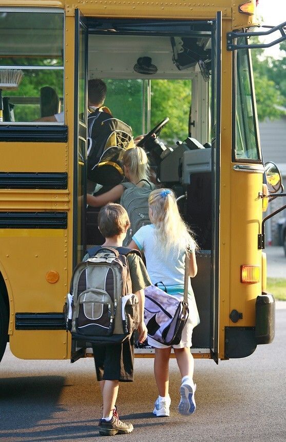 Children with backpacks getting on a school bus.